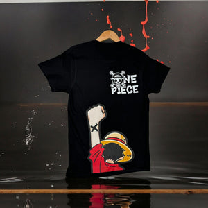T-shirt nera One Piece con stampa di Luffy e logo Mugiwara, appesa su sfondo scuro.