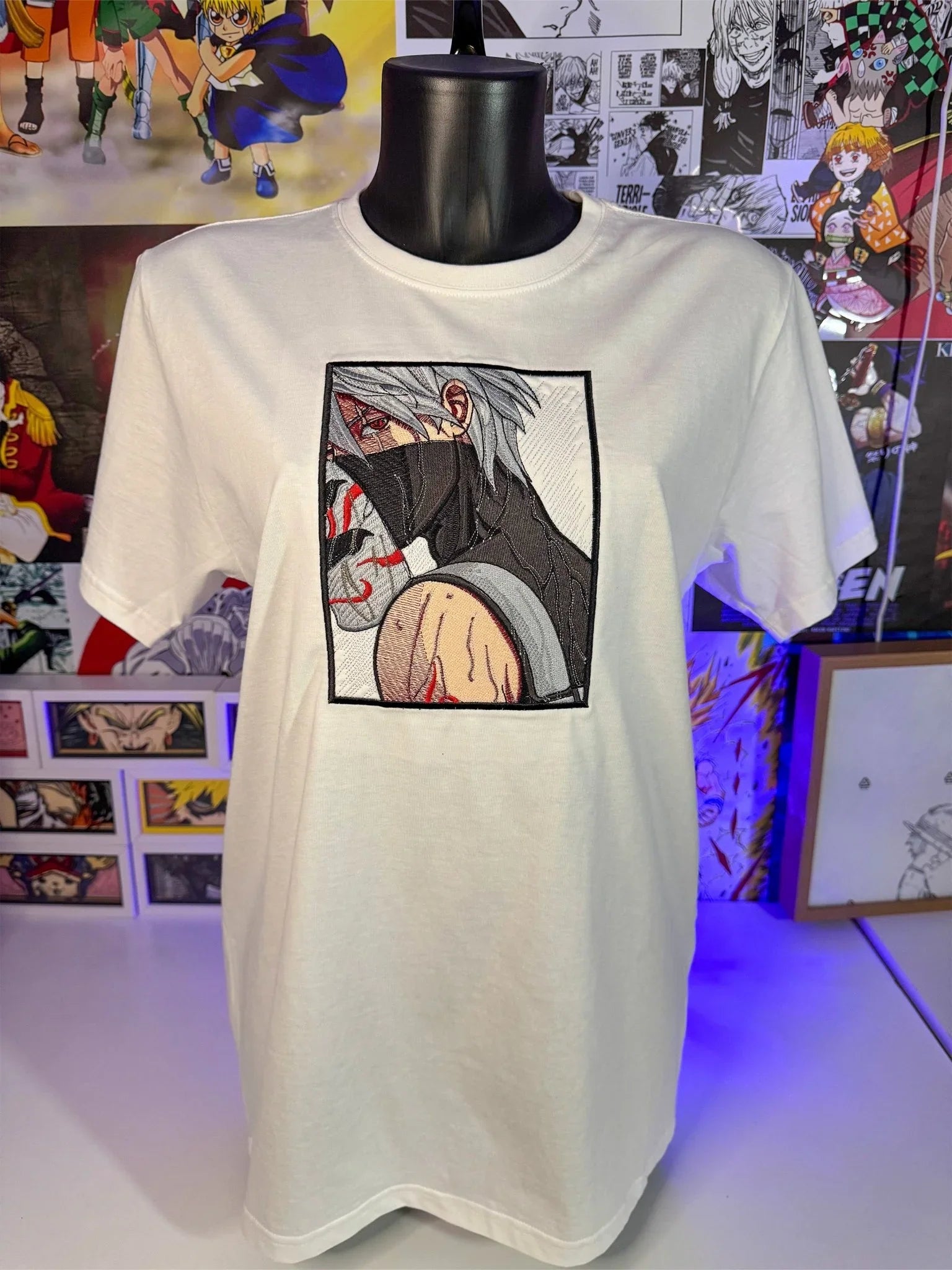 T-shirt bianca anime ricamata con personaggio mascherato, stile manga giapponese, esposta su manichino.